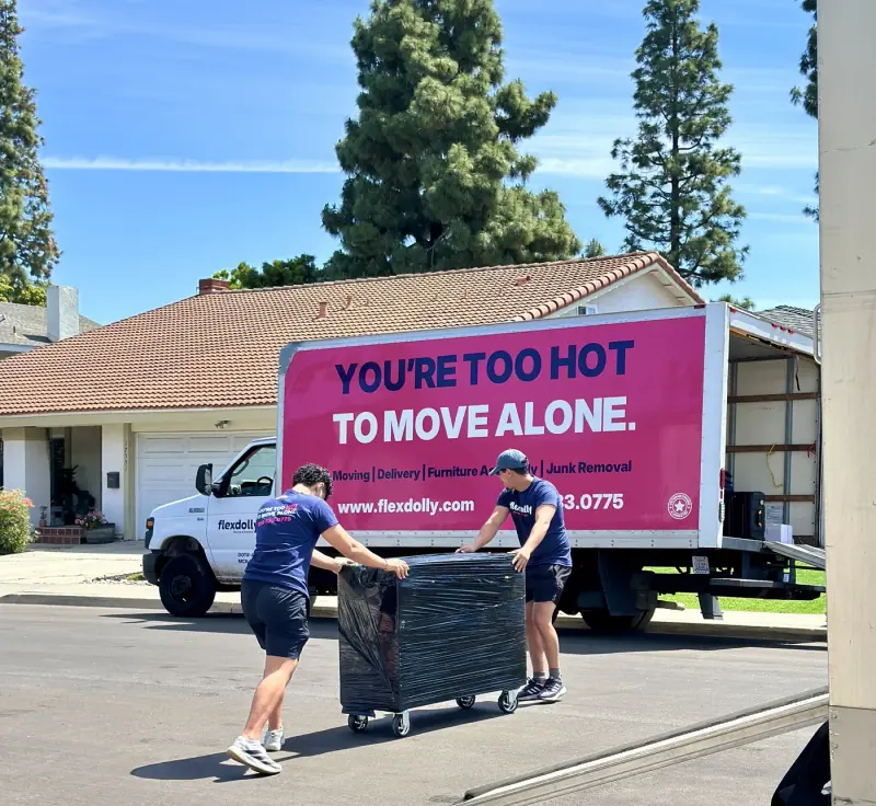 Two Flexdolly movers wheeling a shrink-wrapped dresser out to the truck