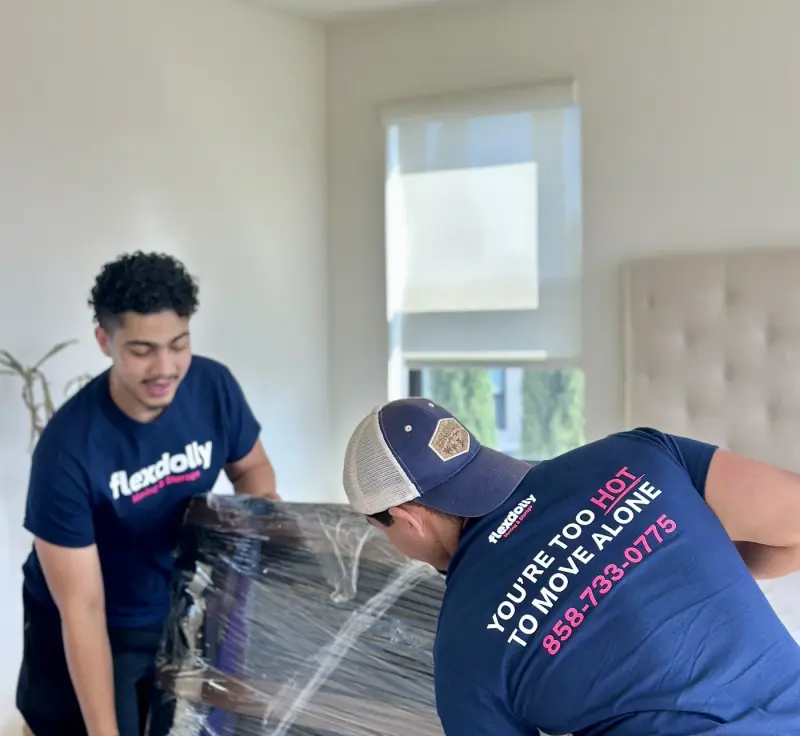Two Flexdolly movers shrink-wrapping a mattress in a bedroom