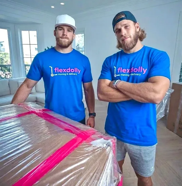 Two Flexdolly movers carrying furniture fully wrapped in pink shrink-wrap