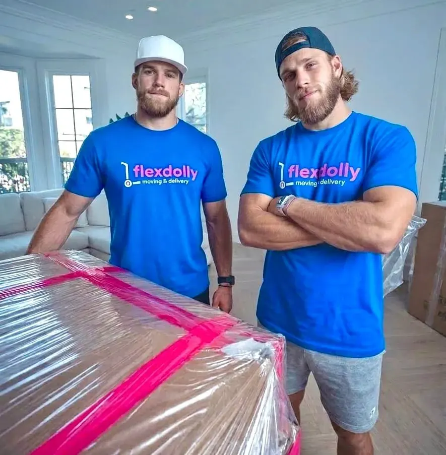 Two Flexdolly movers carrying furniture fully wrapped in pink shrink-wrap